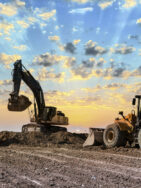 Heavy equipment excavators working on construction site at sunset